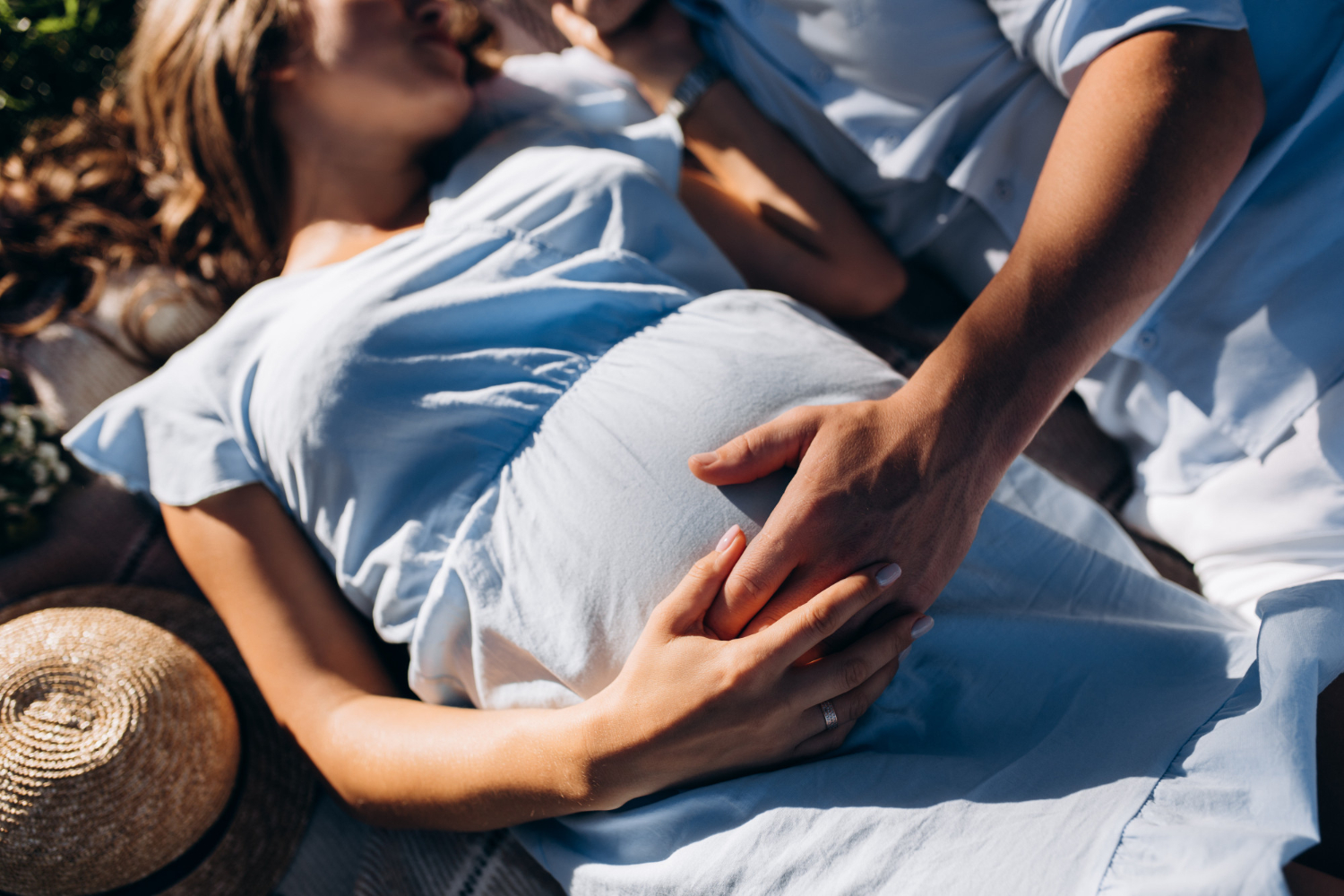 kobieta w ciąży leży na trawie trzymając się dłońmi za brzuch. obok lezy jej partner